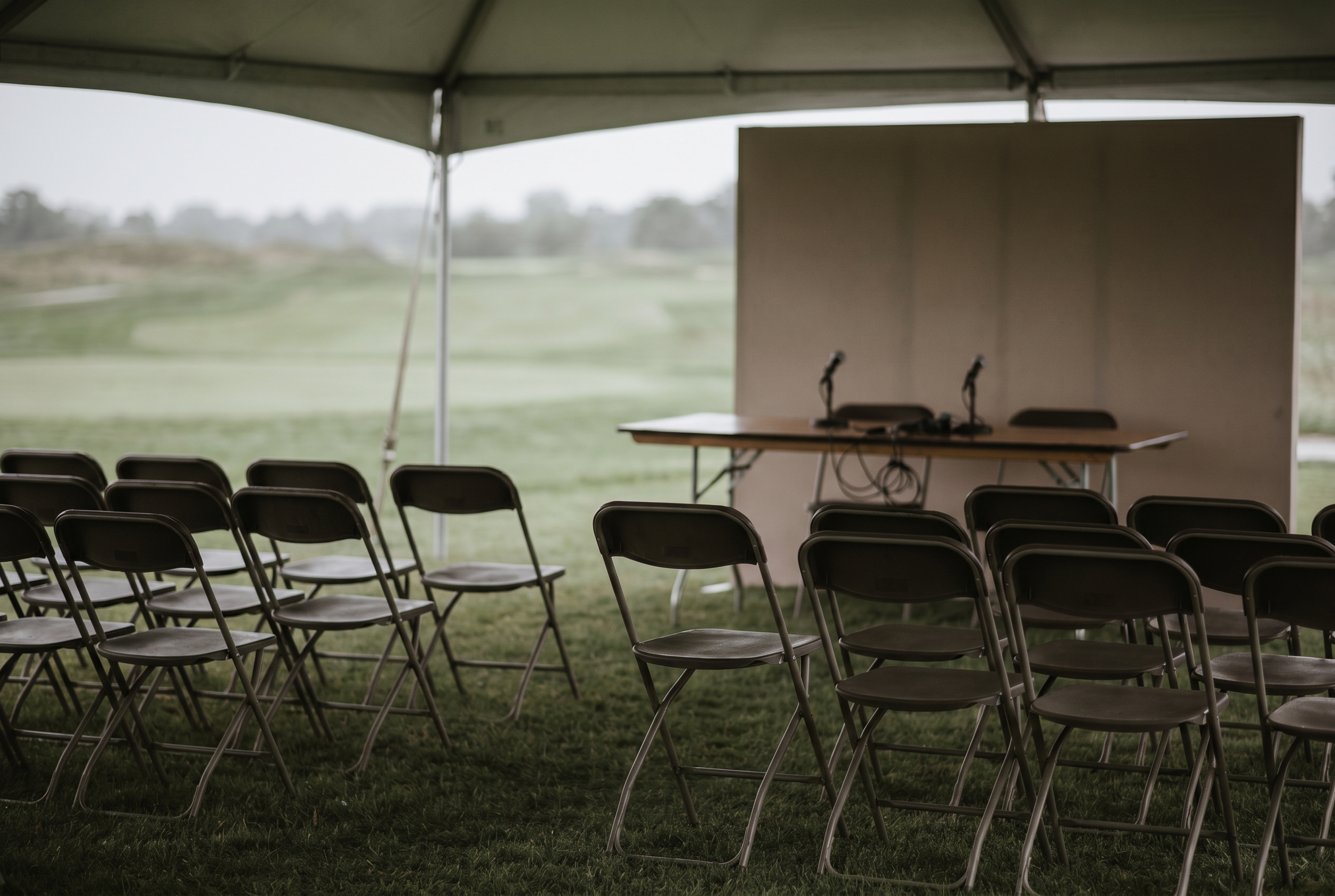 Editorial golf image of empty chairs and a press area beside a course, suggesting off-course business uncertainty